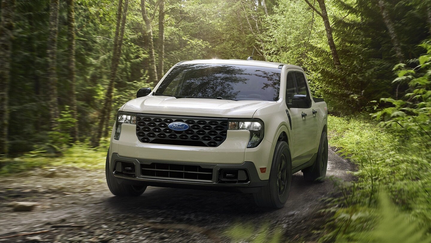 A white Ford Maverick driving on a dirt road through a forest.
