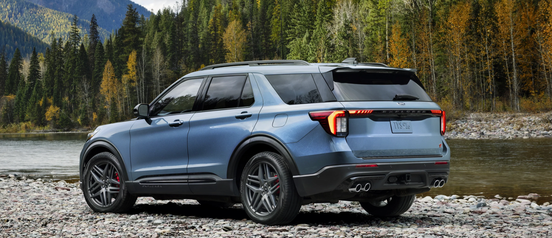 A blue Ford Explorer parked by a river in a forest.