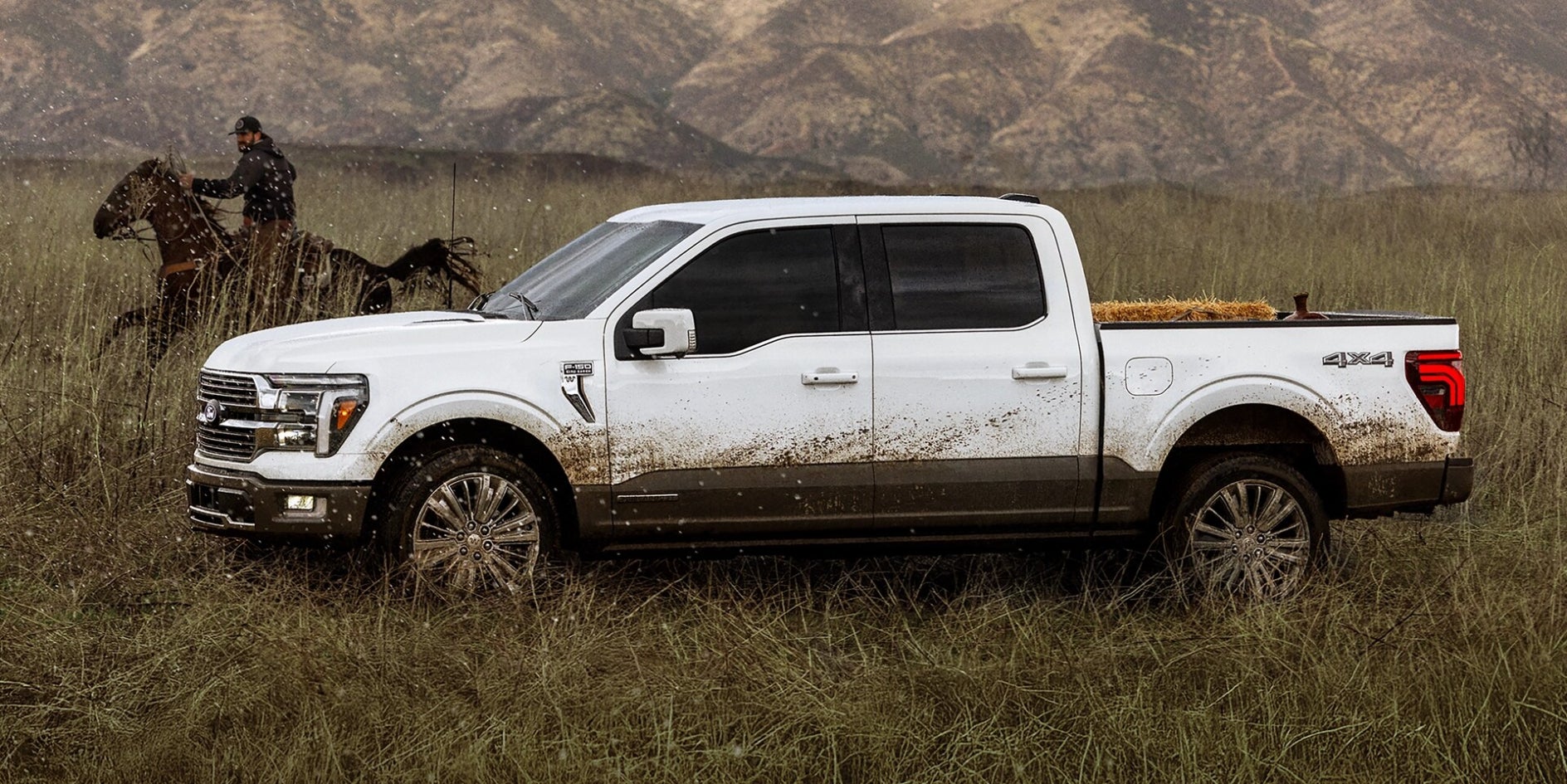 A white Ford F-150 with mud on it driving through a field next to another a man riding a horse.