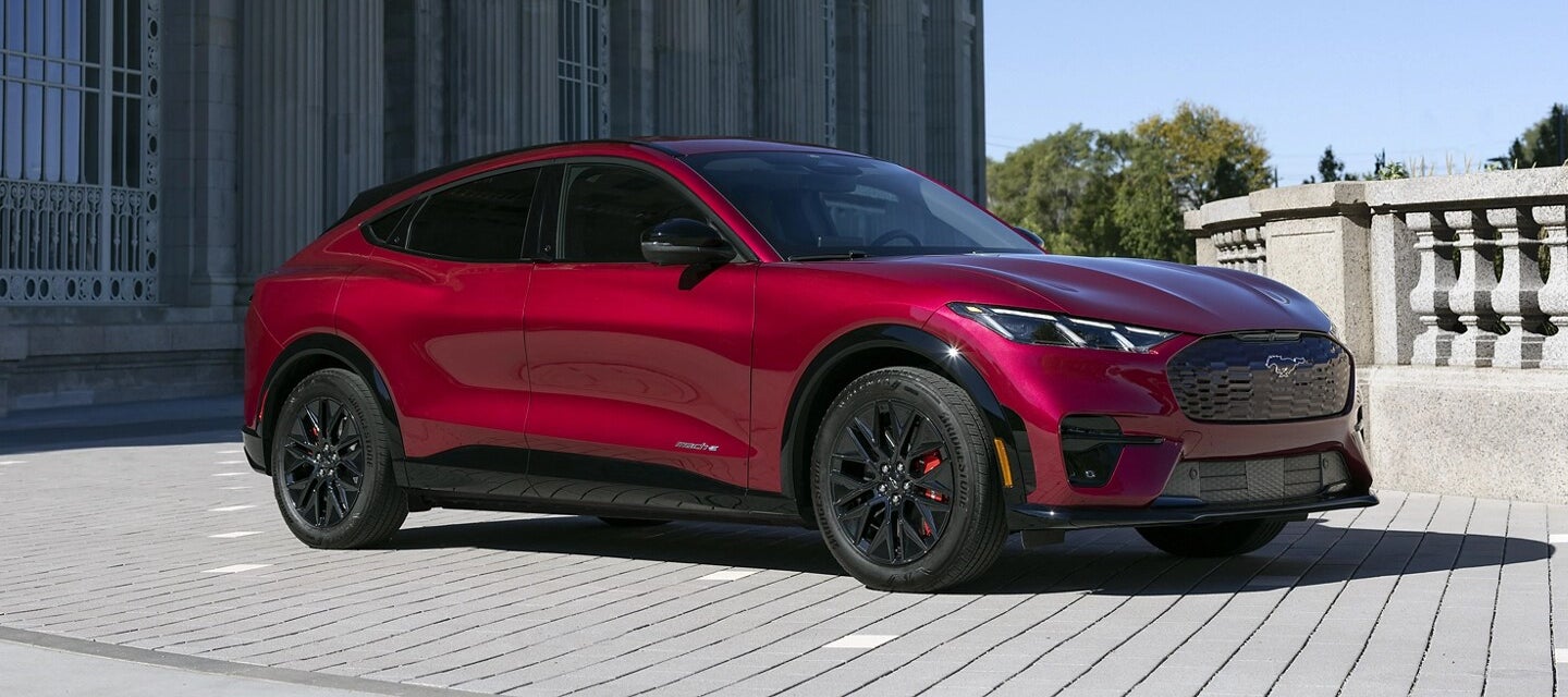 A red Ford Mustang Mach-E parked near an old-looking stone building with columns.
