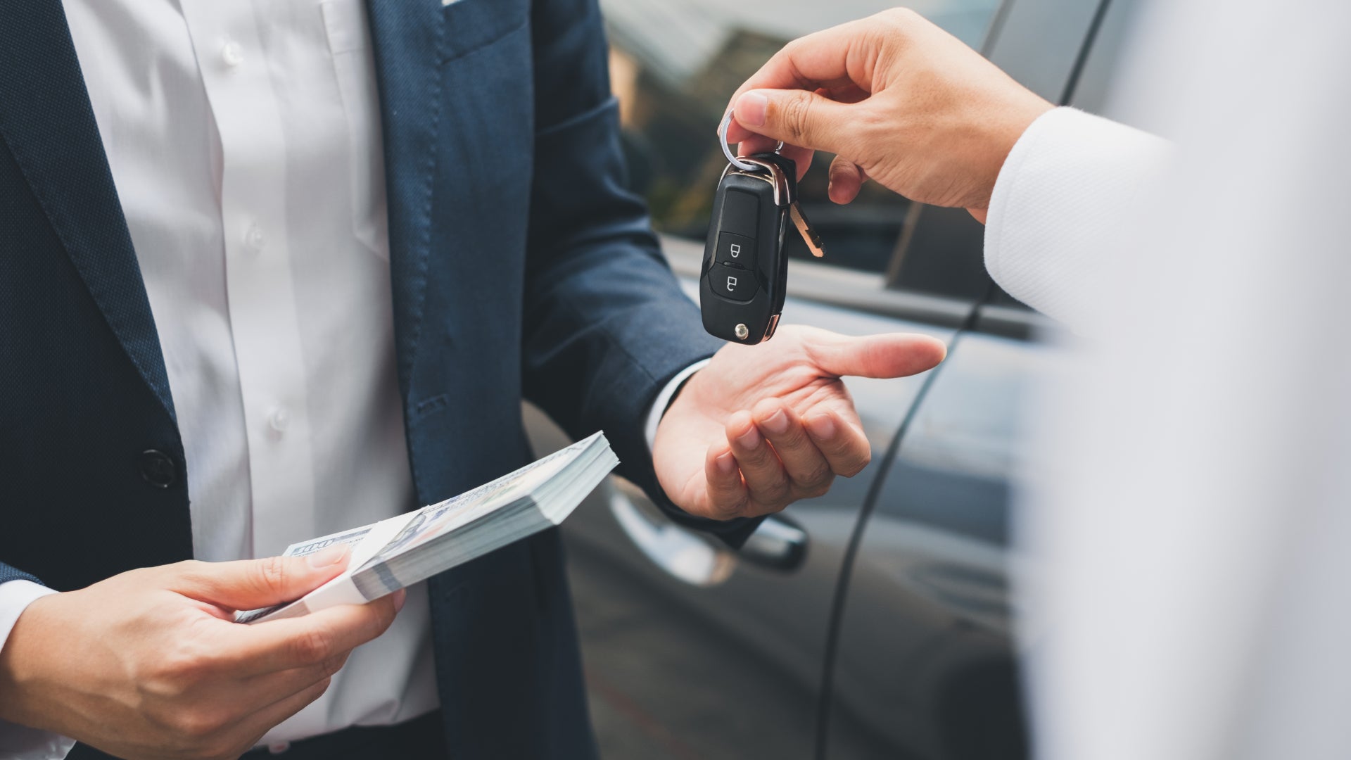 Two people trading money for car keys as one buys a car.