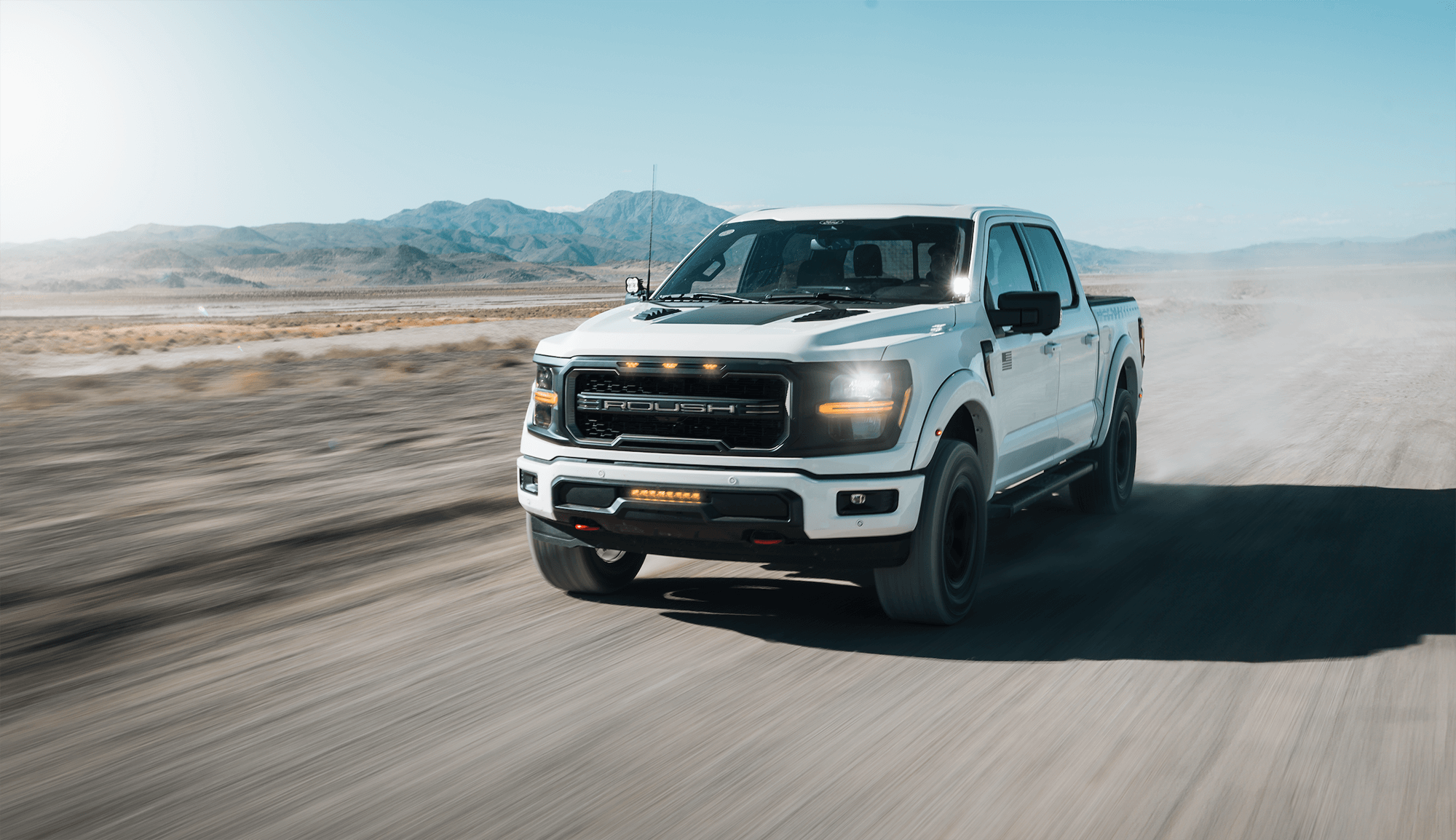 A white Roush Ford F-150 driving through the desert.