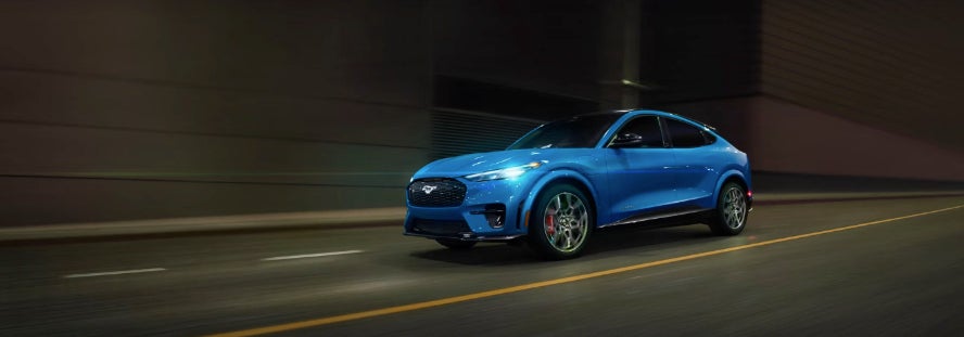 blue Ford Mustang Mach-E electric SUV driving fast on a multi-lane road at night